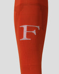 Close up of orange Feyenoord keeper sock showing knit texture and a white emblem on the lower leg